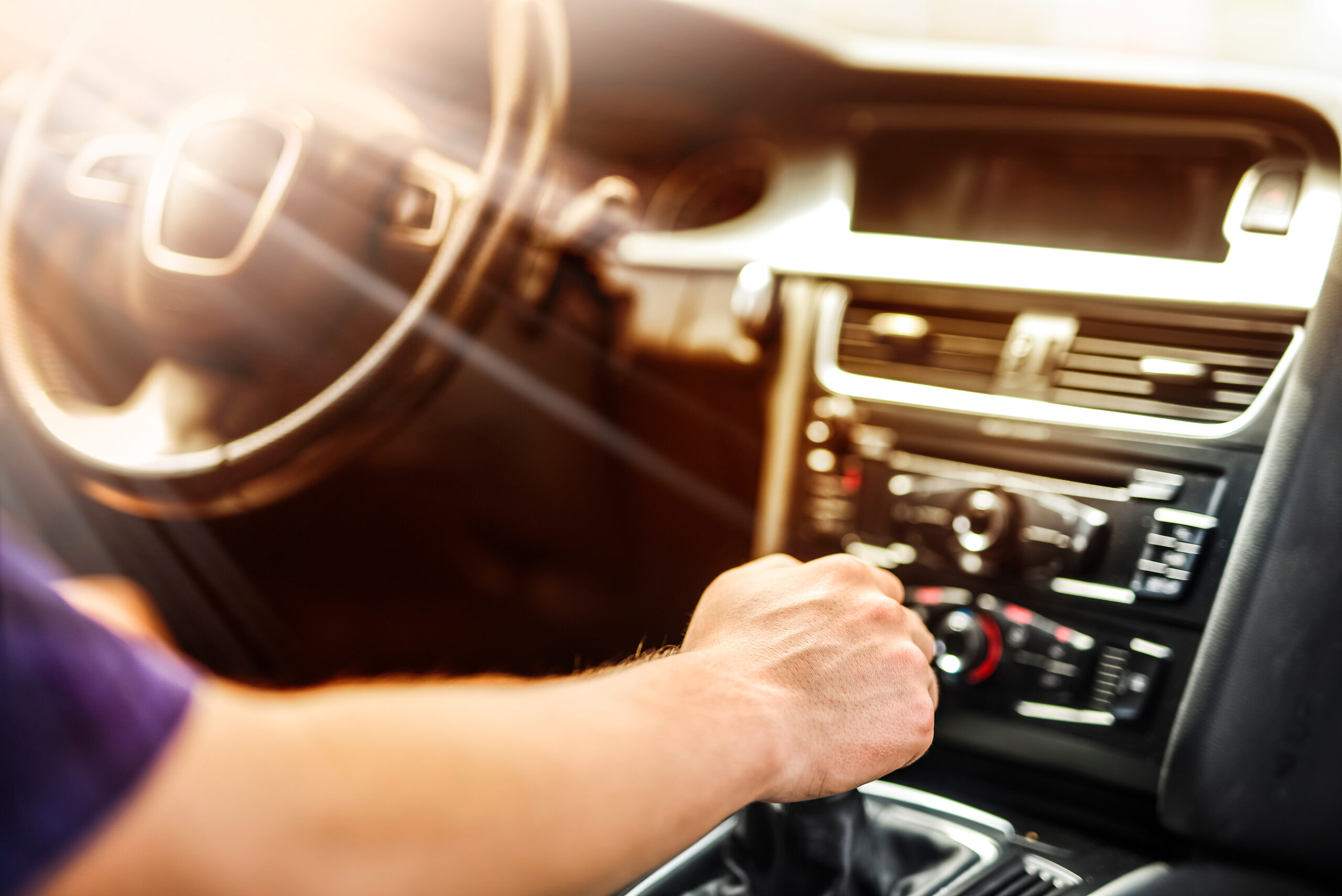 A driver's hand on the gear shifter inside a car, warm sunlight