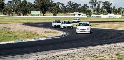 Four small white hatchbacks in a line through a bend