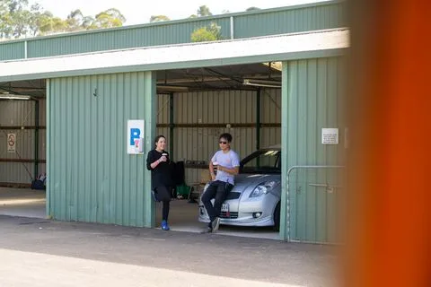 Two people resting in a green garage beside a silver hatchback