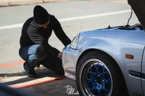 A person crouching to check the front wheel of a silver hatchback