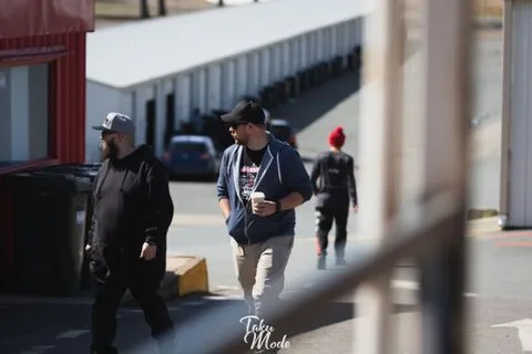 Three people walking past a row of garages, one holding a coffee cup