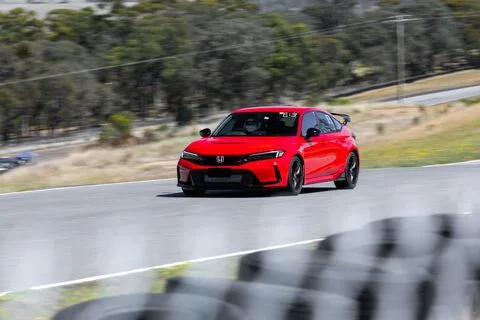 A red hatchback with a rear wing on a bend beyond a blurred tyre wall