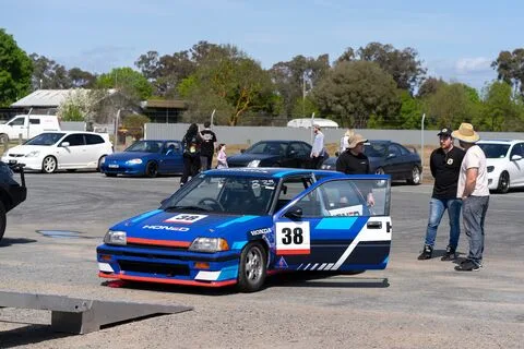 A blue and white Honda hatchback numbered 38 in the paddock with its door open
