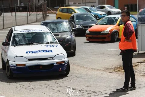 A white Mazda hatchback numbered 707 in the paddock beside a person in an orange vest