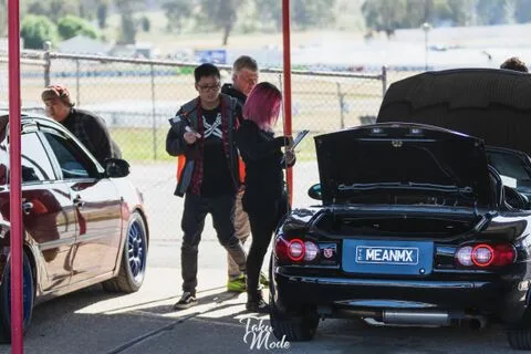 People with clipboards checking a black roadster with its bonnet and boot open